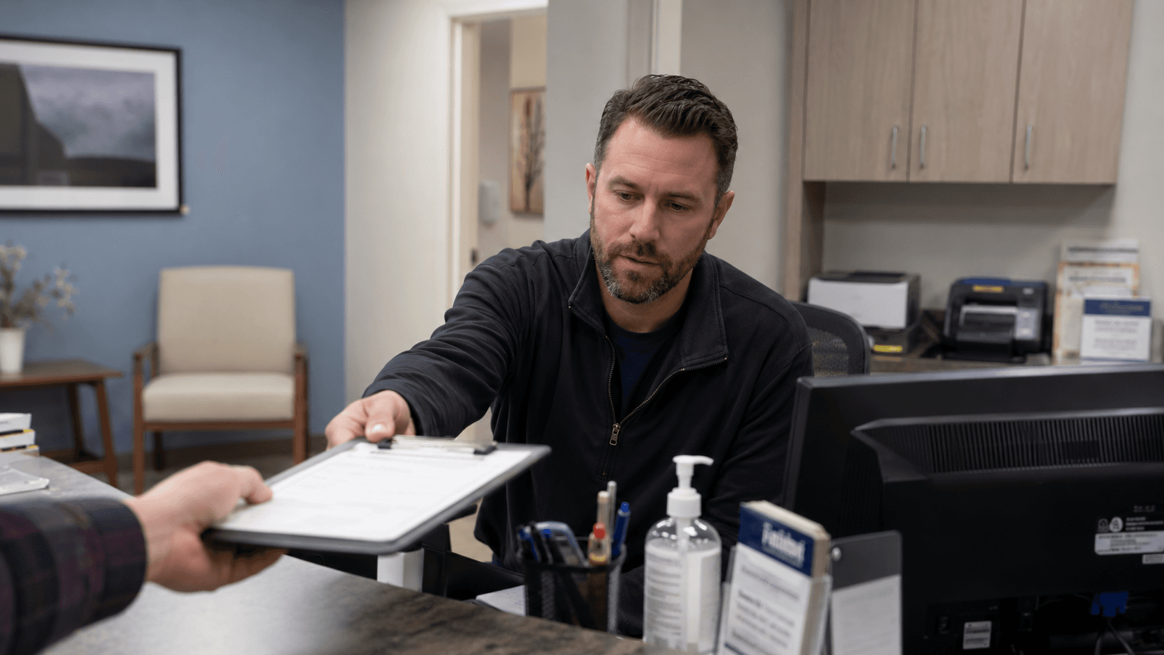 Healthcare office staff member handing a completed document back across the desk during a check-in or compliance workflow