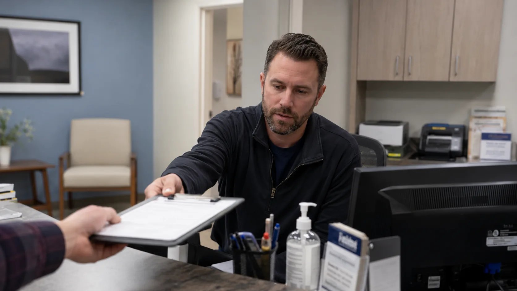Healthcare office staff member handing a completed document back across the desk during a check-in or compliance workflow
